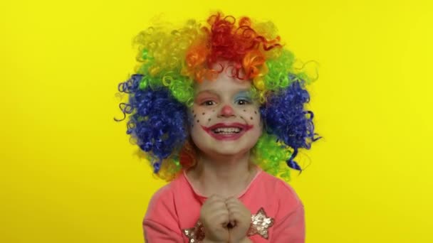 Niña payaso con peluca de arco iris haciendo caras tontas, divirtiéndose, riendo, bailando. Halloween — Vídeos de Stock