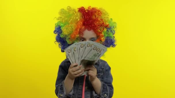 Niño payaso niña en peluca colorida haciendo caras tontas con billetes de dinero en efectivo dólar. Halloween — Vídeo de stock