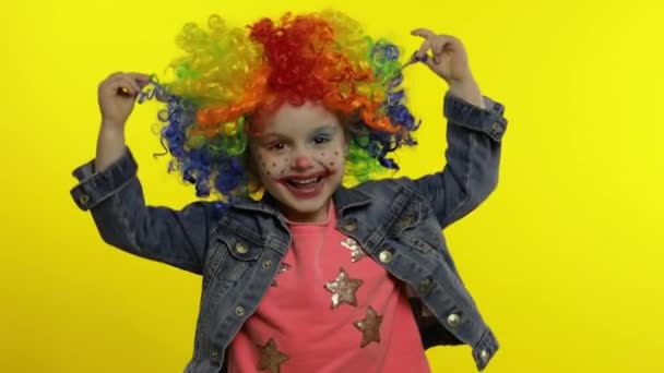 カラフルなウィッグの中の小さな子供の女の子のピエロは愚かな顔を作る。笑顔で踊ってる。ハロウィン — ストック動画