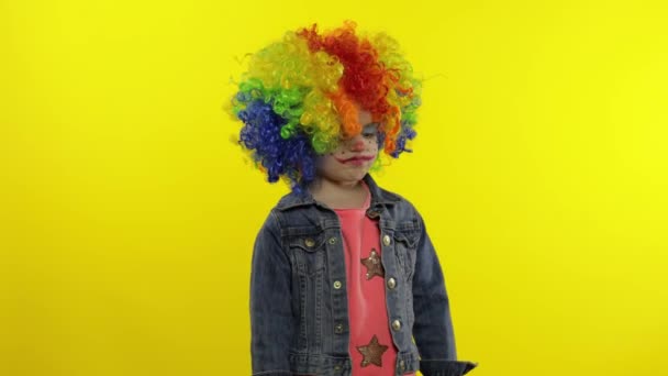 Kleine meisje clown in regenboogpruik boos staand en wachtend op iets. Halloween — Stockvideo