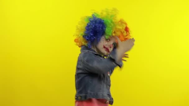 Egy kislány bohóc, színes parókában, buta arcokat vágva. Szórakozni, mosolyogni, táncolni. Halloweeni — Stock videók