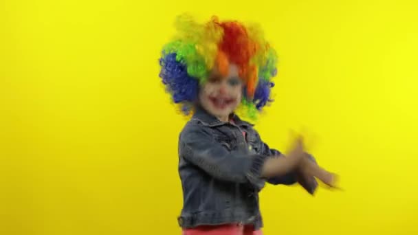 Lille pige klovn i regnbue paryk gør fjollede ansigter, fjolle rundt, smile, danse. Halloween – Stock-video