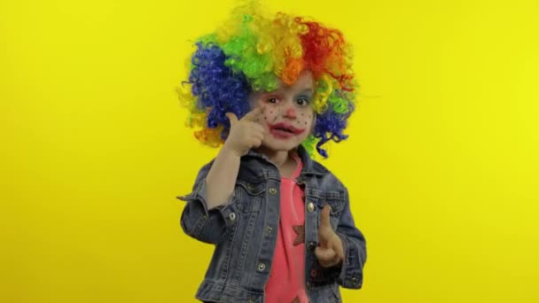 Niña payaso con peluca de arco iris haciendo caras tontas, cantando, sonriendo, bailando. Halloween — Vídeo de stock