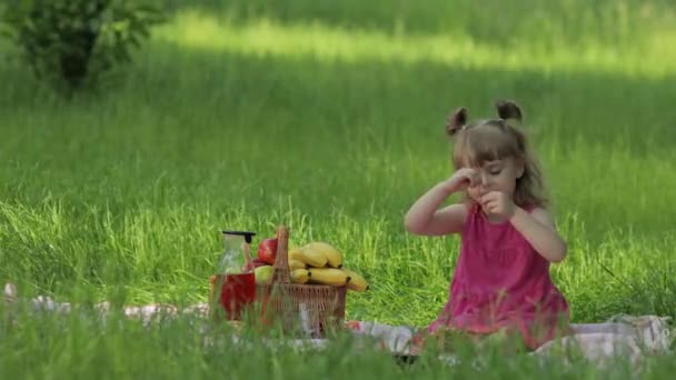 Fin de semana en el picnic. Preciosa niña caucásica en prado de hierba verde comiendo alegre, cereza — Vídeo de stock