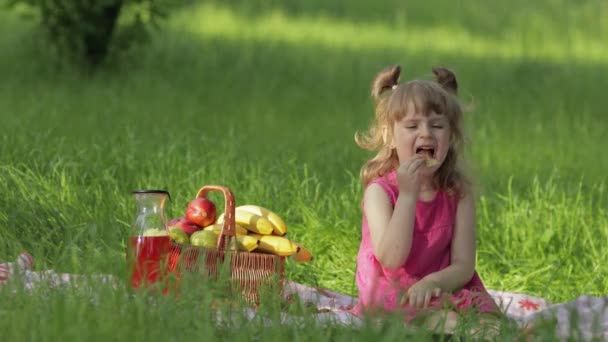 Helg på picknick. Kaukasiska barn flicka på gräs äng med korg full av frukt. Pannkakor — Stockvideo