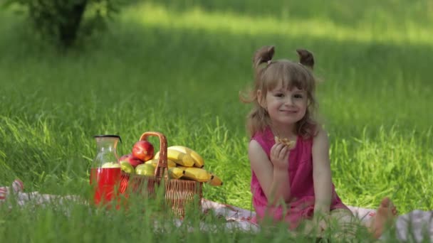 Fim de semana no piquenique. Menina branca no prado de grama com cesta cheia de frutas. Comer panquecas — Vídeo de Stock