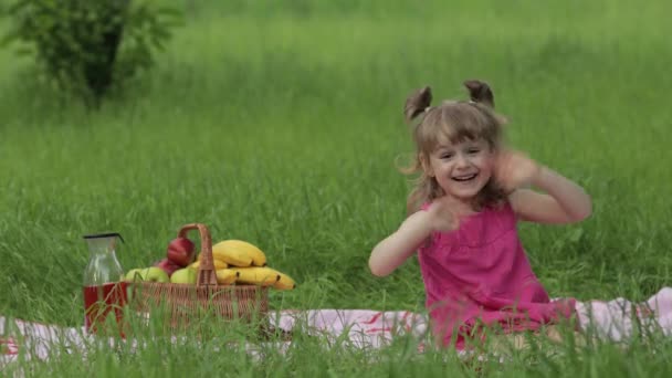 Víkend na pikniku. Krásné kavkazské dítě dívka na zelené trávě louka sedět na přikrývce mává rukama — Stock video