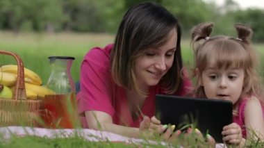 Aile pikniği. Annesiyle birlikte kız çocuğu tabletle online oyun oynuyor. Sohbet.