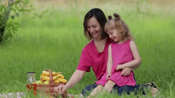 Сімейні вихідні на пікніку. Дочка дівчинка з матір'ю на лузі їсть веселий, вишневий — стокове відео