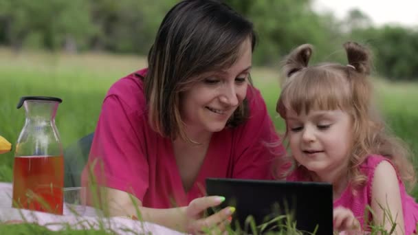 Un picnic in famiglia. Figlia bambina con madre studia lezioni su tablet. Istruzione a distanza — Video Stock