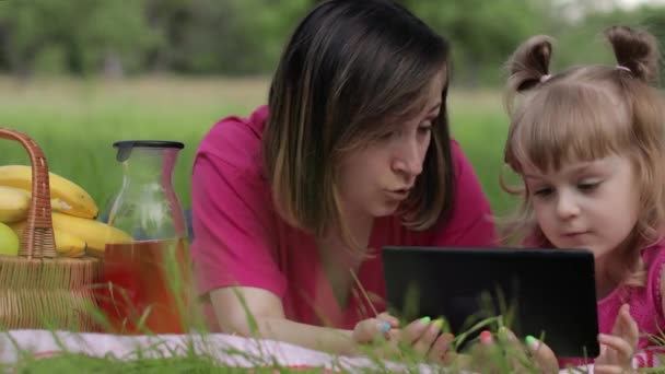 Un picnic in famiglia. Figlia bambina con madre studia lezioni su tablet. Istruzione a distanza — Video Stock