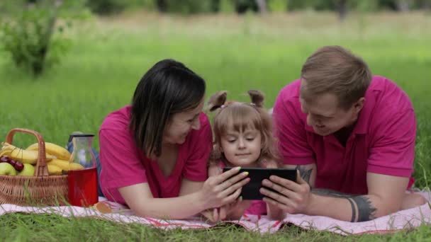 Family weekend picnic. Daughter child girl with mother and father play online games on tablet — Stock Video