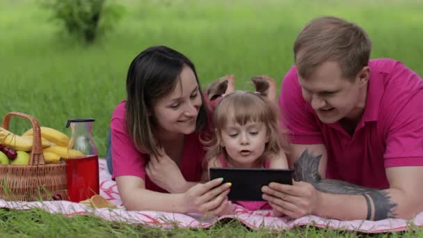 Um piquenique de fim de semana. Filha menina criança com mãe e pai assistindo filmes on-line no tablet — Vídeo de Stock