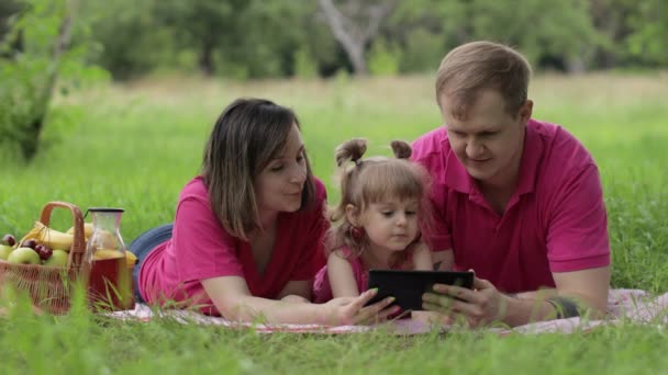 家庭周末野餐。与父母一起在平板电脑上观看在线电影的女儿 — 图库视频影像