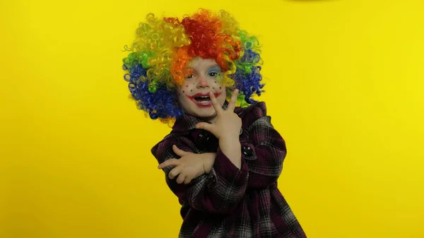 Niña payaso en peluca colorida haciendo caras tontas, divirtiéndose, sonriendo, bailando. Halloween —  Fotos de Stock