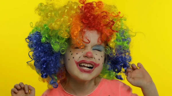 Kleine Kinderclownin mit bunter Perücke, die alberne Gesichter macht, Spaß hat, lächelt, tanzt. Halloween — Stockfoto