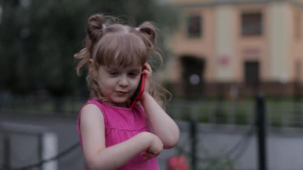 Παιδί κορίτσι μιλάμε από smartphone σε εξωτερικούς χώρους. Παιδί με ροζ φόρεμα μιλάει από κινητό τηλέφωνο στο δρόμο της πόλης — Αρχείο Βίντεο
