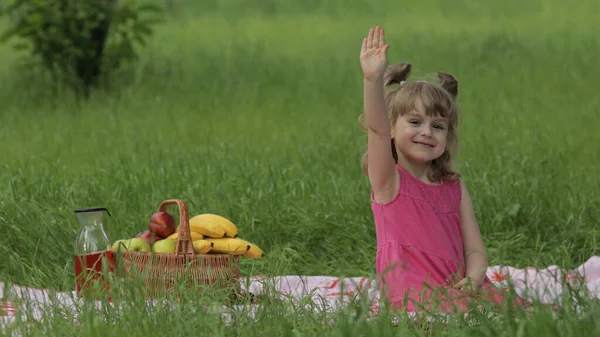 Weekend na pikniku. piękny biały dziecko dziewczyna na zielony trawa łąka siedzieć na koc machając jej ręce — Zdjęcie stockowe