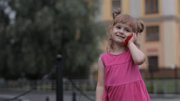 Kind meisje praten met de smartphone buiten. Kind in roze jurk praten door mobiele telefoon op straat — Stockfoto