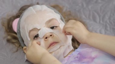 Genç kız nemlendirici yüz maskesi takıyor. Çocuk cildine kozmetik maskeyle bakıyor.