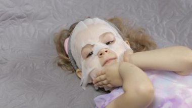 Genç kız nemlendirici yüz maskesi takıyor. Çocuk cildine kozmetik maskeyle bakıyor.