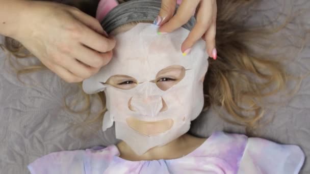 Adolescente meninas mãe aplicando máscara facial hidratante na filha. Criança com máscara de pele facial cosmética — Vídeo de Stock