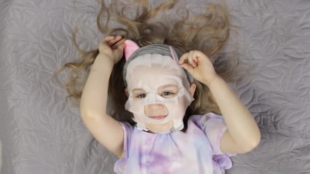 Дівчина-підліток наносить зволожуючу маску для обличчя. Дитина доглядає за шкірою за косметичною маскою для обличчя — стокове відео