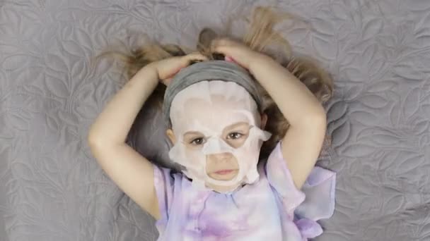 Tiener meisje met hydraterende gezichtsmasker. Kind kind verzorgen van de huid met cosmetische gezichtsmasker — Stockvideo