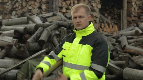 Lumberjack in reflective jacket. Man woodcutter hold huge axe. Sawn logs, firewood background — Stock Video