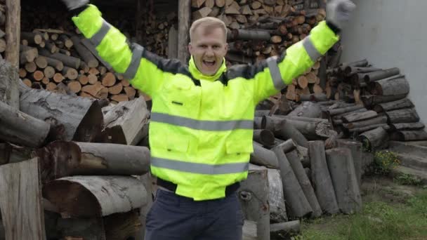 Dřevorubec v reflexní bundě. Muž dřevorubec tančí, slaví. Pilařská kulatina, zázemí z palivového dřeva — Stock video