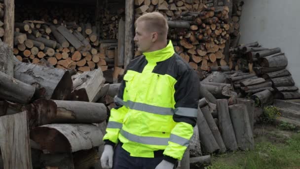 Taglialegna in giacca riflettente. L'uomo taglialegna mostra il pollice in alto. Tronchi segati, sfondo legna da ardere — Video Stock