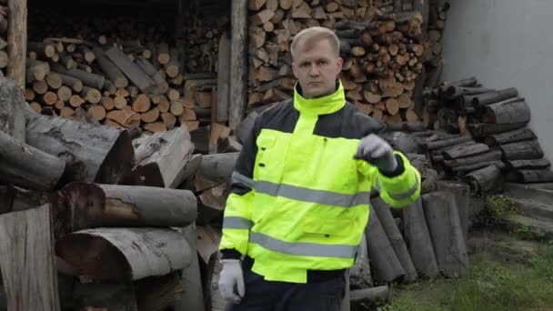 Lumberjack em casaco reflexivo. Homem lenhador mostrar sinal ok. Toros serrados, fundo de lenha — Vídeo de Stock