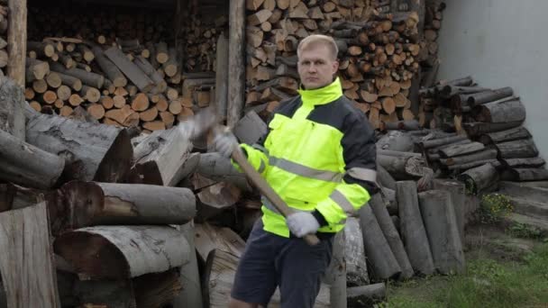 Skogshuggare i reflekterande jacka. Man hugger ved med stor yxa. Sågade stockar, ved bakgrund — Stockvideo