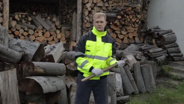 Lumberjack en chaqueta reflectante. Hombre leñador con hacha grande. Troncos aserrados, fondo de leña — Vídeos de Stock
