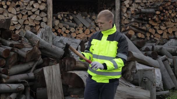 Lumberjack en chaqueta reflectante. El leñador sostiene un hacha pequeña, muestra una señal aceptable. Troncos aserrados, leña — Vídeo de stock