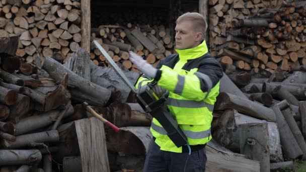 Skogshuggare i reflekterande jacka. En träskärare med elektrisk motorsåg. Sågade stockar, ved, sågverk — Stockvideo