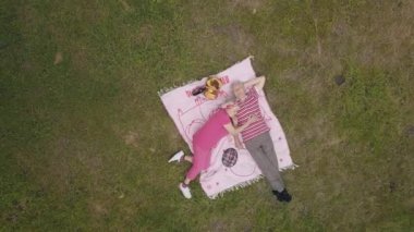 Hafta sonu parkta aile pikniği. Hava görüntüsü. Yaşlı çift yeşil çayırda battaniyeye uzanıyor.