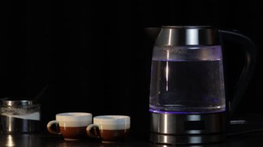 Bardakta kaynamış su, şeffaf elektrikli su ısıtıcısı ve mavi ışık aydınlatma. Siyah arkaplan