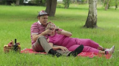 Hafta sonu parkta aile pikniği. Yaşlı bir çift battaniyeye oturur ve şarap içer. Öpüşmek. Aşk