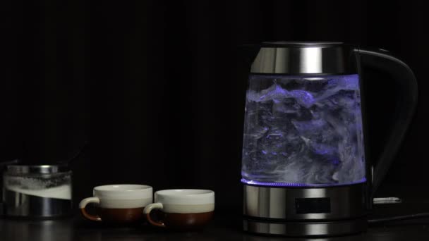 ガラスの透明電気ケトルに青い照明で水を沸かします。黒の背景 — ストック動画