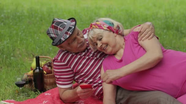 Семейный пикник. Старшие бабушка и дедушка пара в парке с помощью смартфона онлайн просмотра, чат — стоковое видео