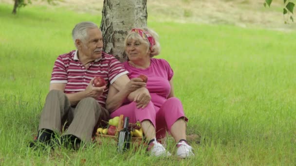 Familjelweekend picknick i parken. Aktiva äldre kaukasiska par sitta på filt och äta frukt — Stockvideo