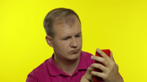 Junger kaukasischer Mann posiert in rosa T-Shirt. Schöner Kerl mit Handy und gewinnen Sie etwas — Stockvideo