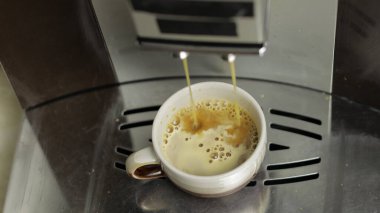 Kahve makinesinden küçük beyaz ve kahverengi bardakta espresso fışkırıyordu. Kapat.