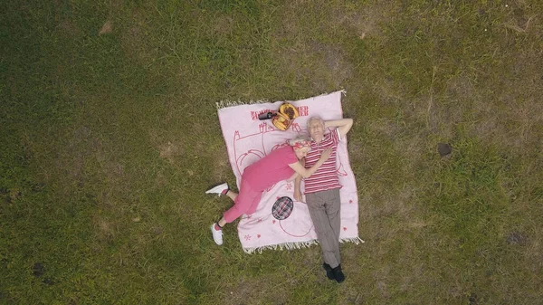 Picnic familiar de fin de semana en el parque. Vista aérea. Senior pareja de edad se encuentran en la manta en el prado de hierba verde —  Fotos de Stock