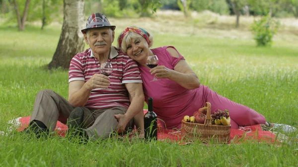 Week-end pique-nique en famille dans le parc. Actif vieux couple caucasien assis sur la couverture et boire du vin — Photo