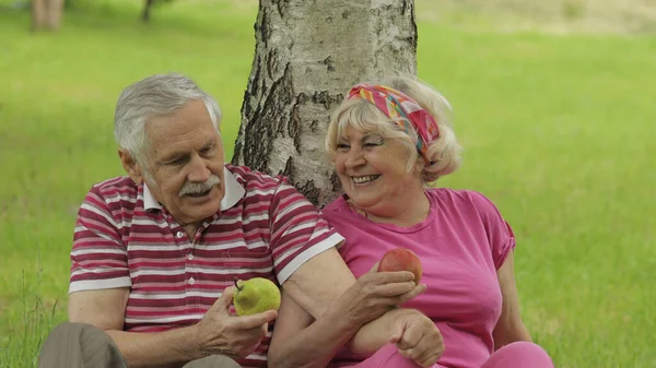 Семейный пикник в парке. Активная пожилая кавказская пара сидит на одеяле и ест фрукты — стоковое фото