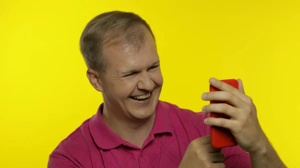 Fiatalember, rózsaszín pólóban pózol. Jóképű srác mobiltelefont használ, vicces videókat néz online — Stock Fotó
