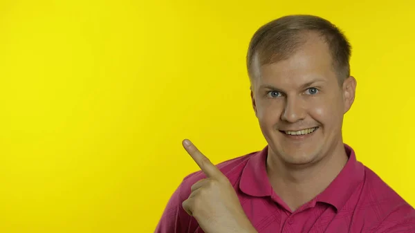 Portret van een jonge man die poseert in een roze t-shirt. Gelukkig lachende man wijzend naar iets met de hand — Stockfoto
