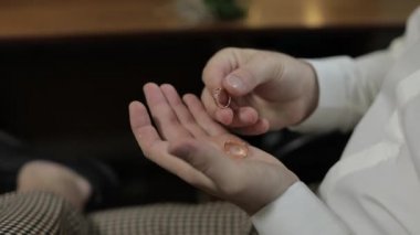 Beyaz gömlekli damat avucunun içinde alyanslar tutuyor. Adam yüzüklere dokunuyor.